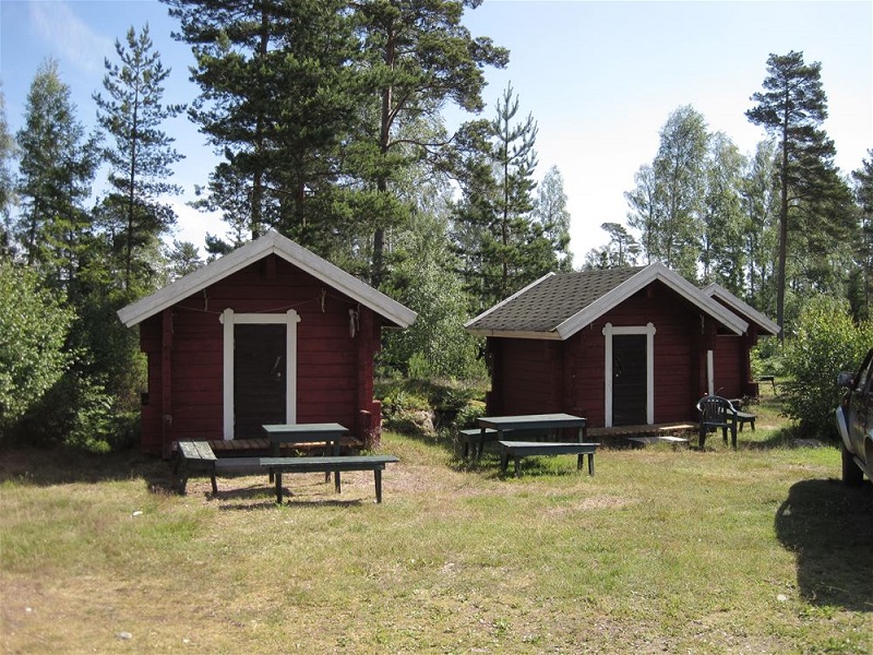 Röda tvåbäddsstugor med utebord bland tallarna på Svinö